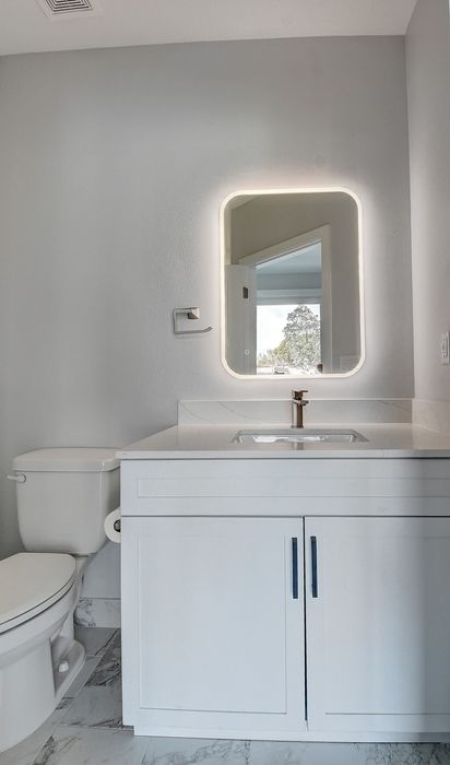Modern bathroom with sleek white vanity, elegant marble flooring, and a stylish LED-lit mirror.