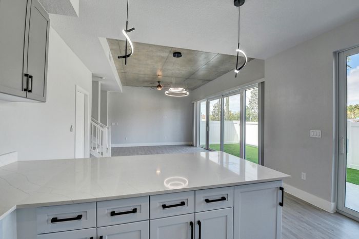 Contemporary open-concept living space featuring a sleek kitchen island, modern lighting fixtures, and expansive glass doors leading to a serene outdoor view.