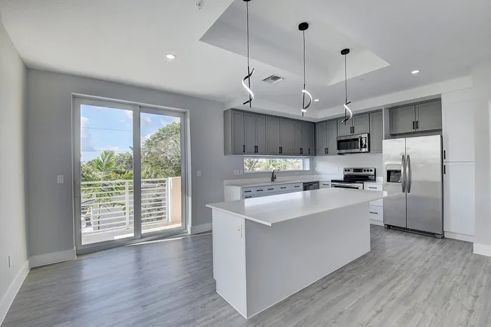 Contemporary kitchen with sleek grey cabinetry, stainless steel appliances, and a large island, complemented by modern pendant lighting and ample natural light through sliding glass doors.
