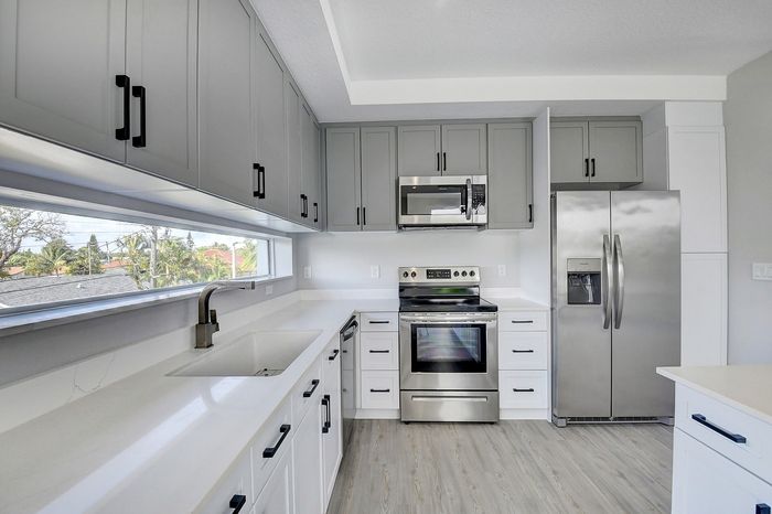Modern kitchen with sleek stainless steel appliances, elegant gray cabinetry, and large window offering natural light.