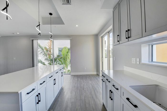 Sleek modern kitchen with elegant white cabinetry, large island, and ample natural light from floor-to-ceiling windows overlooking lush greenery.