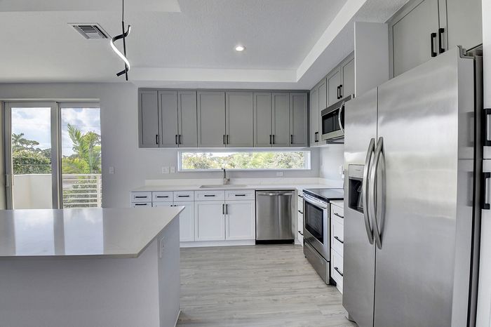 Modern kitchen with sleek stainless steel appliances, elegant gray cabinets, and expansive windows showcasing lush green views.