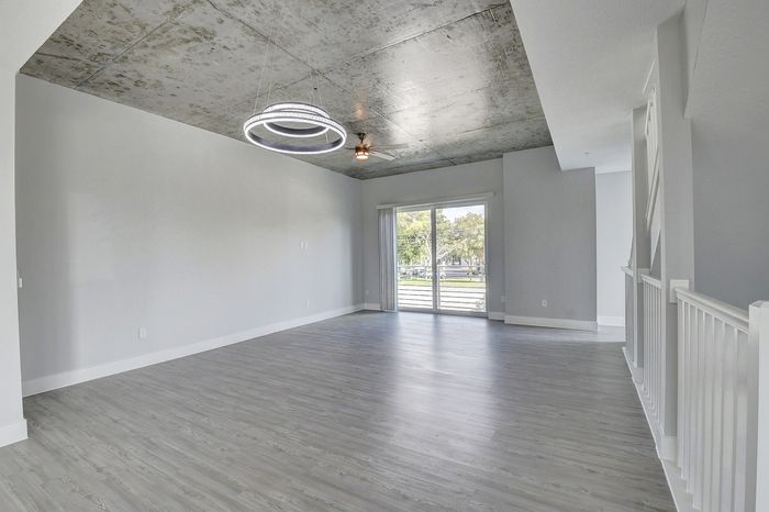 Sleek modern apartment with open floor plan, featuring polished wood floors, a trendy concrete ceiling, and abundant natural light from large sliding glass doors.