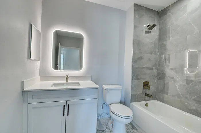 Modern bathroom with sleek marble tile, illuminated mirror, elegant fixtures, and a spacious bathtub for relaxation.