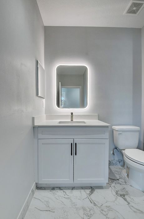 Contemporary bathroom featuring sleek white cabinetry, elegant marble flooring, and a modern backlit mirror.