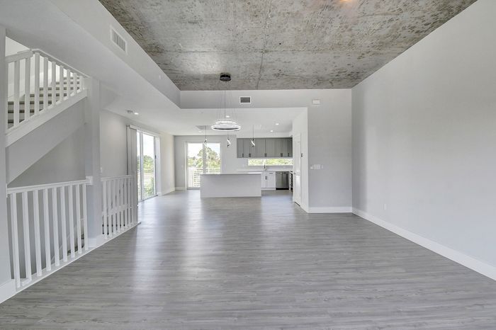 Sophisticated open-concept apartment with modern kitchen, high ceilings, gray wooden floors, and elegant fixtures.