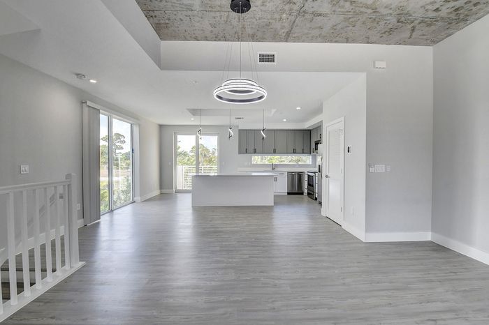 Contemporary open-plan living area with sleek modern kitchen, stylish pendant lighting, and expansive glass doors leading to a serene balcony view.