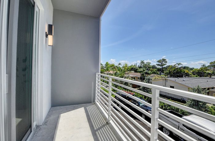 Modern balcony with sleek white railing offering a serene view of lush greenery and suburban rooftops under a clear blue sky.