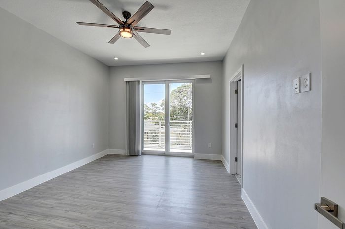 Bright, modern room featuring sleek wood flooring, a stylish ceiling fan, and large sliding doors leading to a balcony with a scenic view.