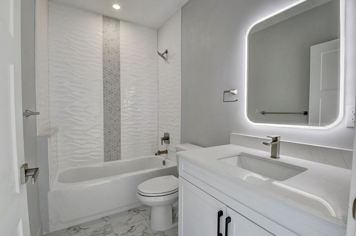 Modern bathroom featuring elegant textured wall tiles, illuminated mirror, and sleek fixtures for a luxurious feel.