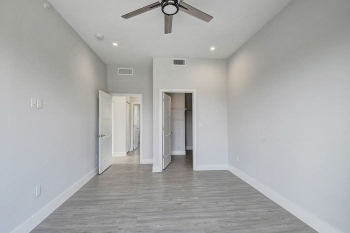Bright, spacious room with modern gray flooring, a sleek ceiling fan, and closet space, perfect for a stylish living area.