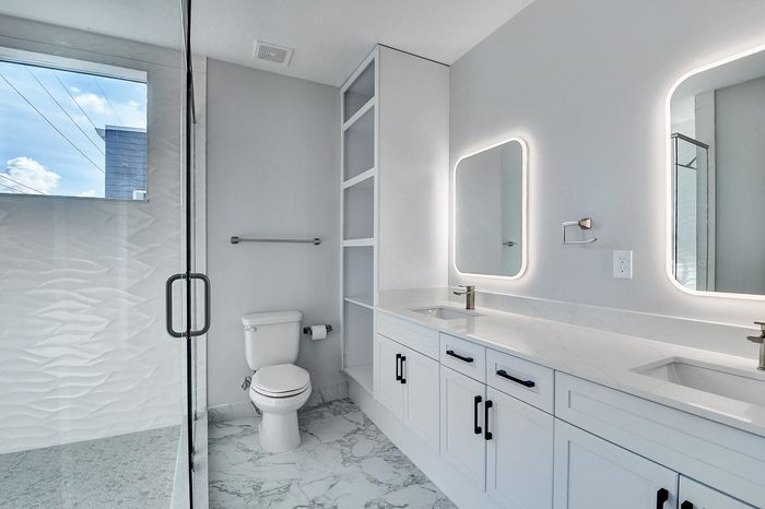 Sleek modern bathroom featuring dual vanities with illuminated mirrors, elegant white cabinetry, and a luxurious walk-in shower.