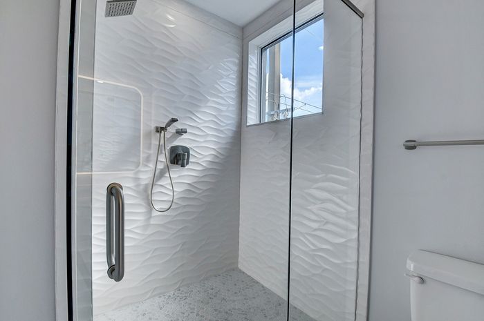Luxurious bathroom with modern textured white wall tiles and a sleek glass shower, filled with natural light.