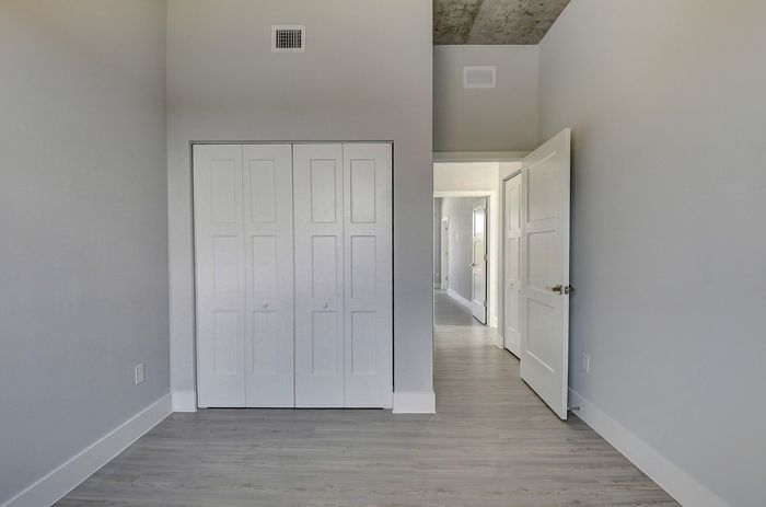 Modern bedroom with sleek grey walls, ample closet space, and a bright hallway leading to other rooms.