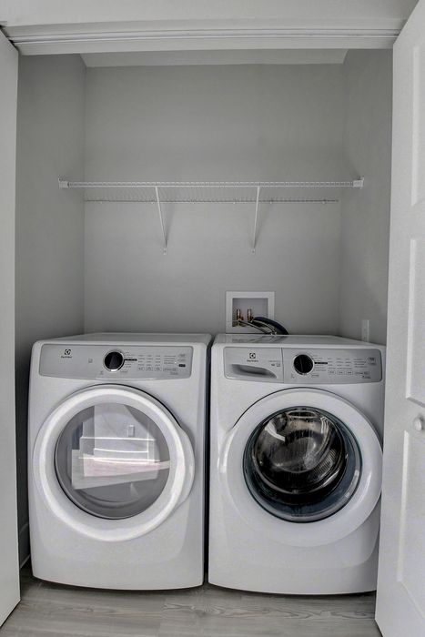 Modern laundry closet featuring a sleek washer and dryer with ample overhead shelving.