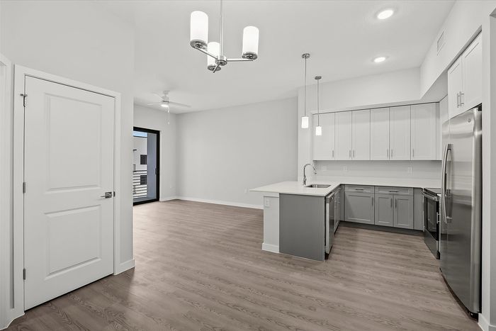 Modern open-concept apartment showcasing a sleek kitchen, elegant lighting, and a bright living area with balcony access.