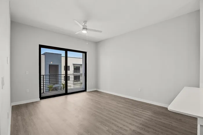 Bright and modern apartment with hardwood floors, large sliding glass doors, and a ceiling fan, offering abundant natural light and access to a private balcony.