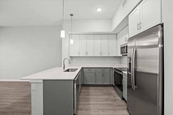Modern kitchen with sleek stainless steel appliances, stylish white cabinetry, and elegant pendant lighting on luxurious wood flooring.