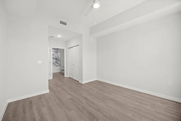 Bright, spacious bedroom with sleek wooden flooring, modern ceiling fan, and direct access to a chic bathroom with marble accents.