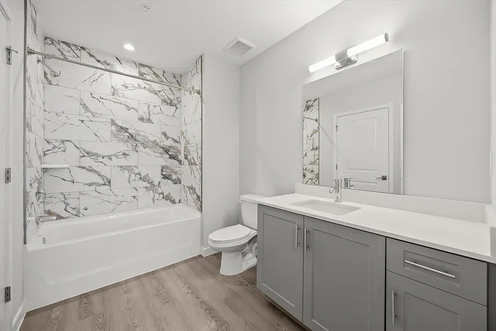 Modern bathroom featuring elegant marble wall tiles, sleek gray cabinetry, and a spacious bathtub.