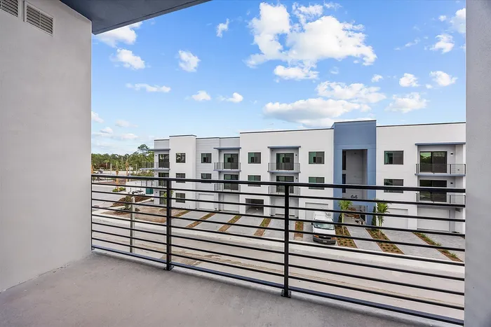 Inviting balcony view overlooking a modern apartment complex with clear blue skies and lush greenery.