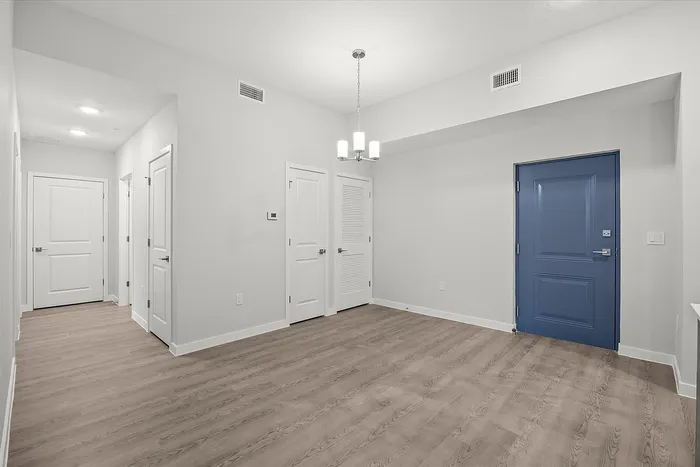 Modern apartment entry area featuring sleek hardwood floors, elegant lighting, and a stylish blue door.
