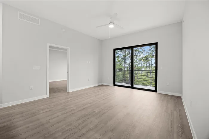 Bright and spacious living area with modern wood flooring and large sliding glass doors leading to a scenic balcony view.