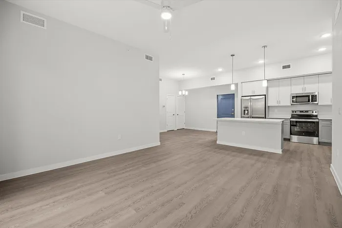 Modern open-concept living area with sleek hardwood floors, a stylish kitchen with stainless steel appliances, and elegant pendant lighting.