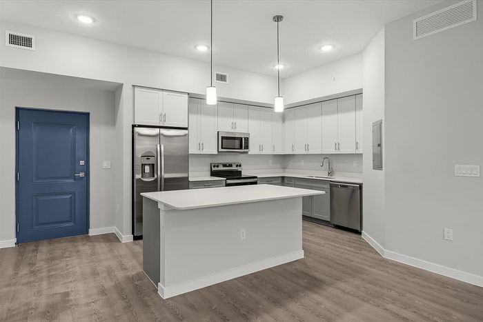 Modern kitchen in a sleek apartment featuring stainless steel appliances, elegant island, and stylish pendant lighting.