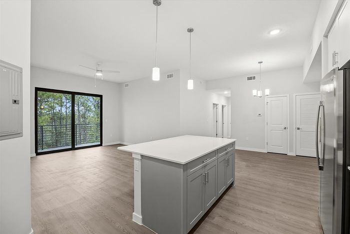 Bright and modern open-concept kitchen with sleek cabinetry, island countertop, and expansive glass doors leading to a scenic balcony view.