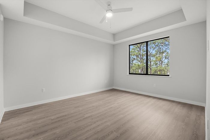 Bright and airy bedroom with sleek wood flooring, modern ceiling fan, and a large window offering picturesque tree views.
