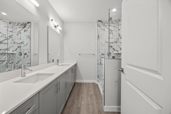 Luxurious bathroom featuring a double vanity with sleek countertops, elegant lighting, and a stylish glass-enclosed shower with marble accents.
