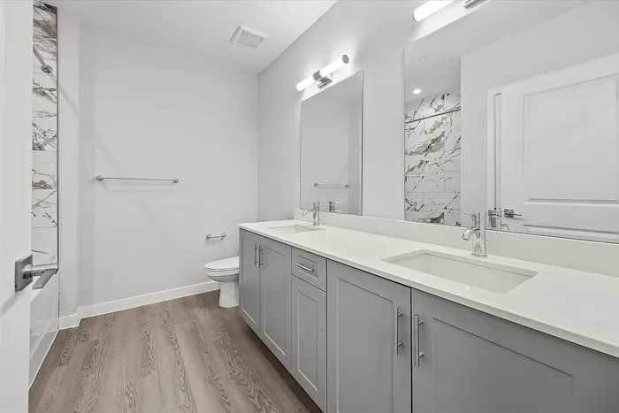 Elegant bathroom with dual sinks, modern gray cabinetry, marble accents, and sleek hardwood flooring.