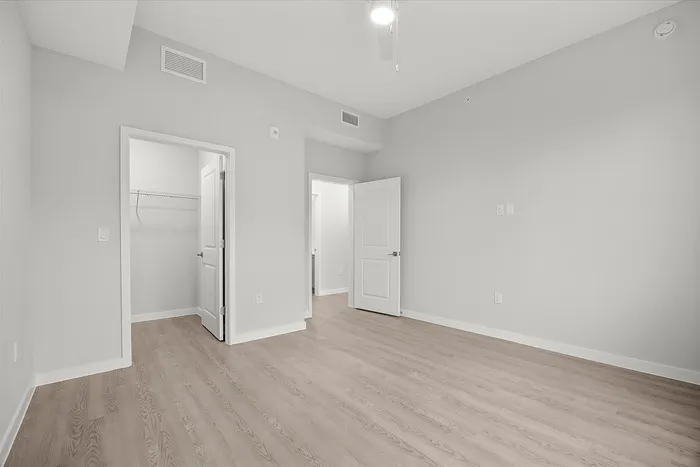 Sleek and modern empty room featuring elegant wood flooring, light gray walls, and a spacious walk-in closet.