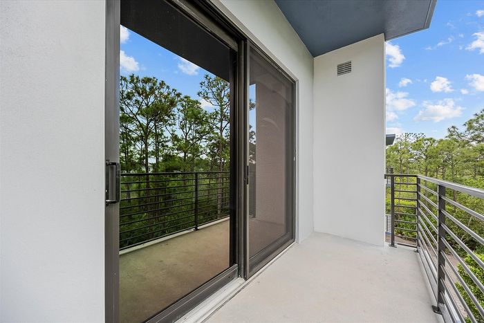 Inviting modern balcony with sleek glass sliding doors overlooking lush green landscape and blue skies.