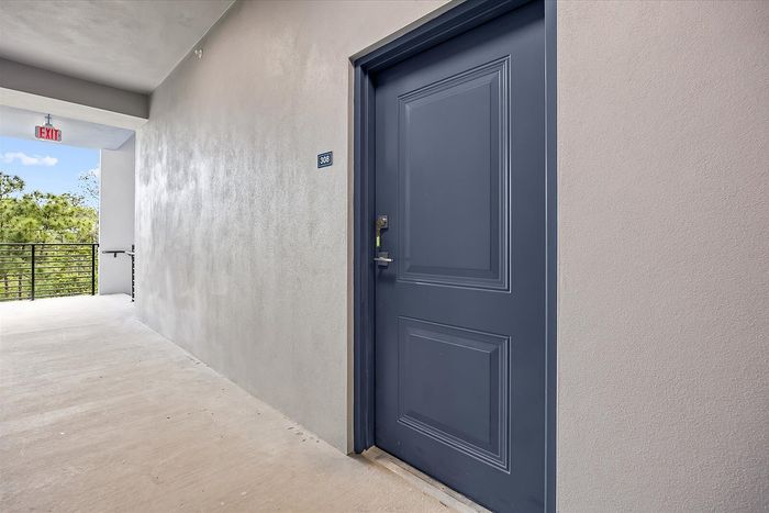 Inviting entrance of an elegant apartment with a sleek navy door and serene outdoor view, offering tranquility and modern charm.