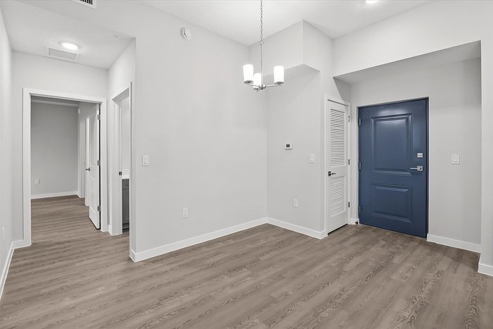 Modern apartment interior with sleek wood flooring, contemporary chandelier, and a stylish blue entry door.