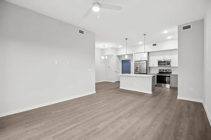 Modern open-concept living space with sleek hardwood floors and a contemporary kitchen featuring stainless steel appliances and chic pendant lighting.