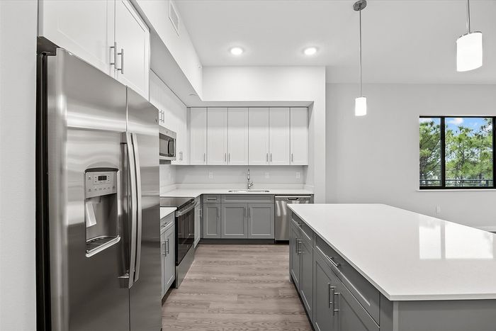 Modern kitchen with sleek stainless steel appliances, elegant pendant lighting, and large window offering natural light.
