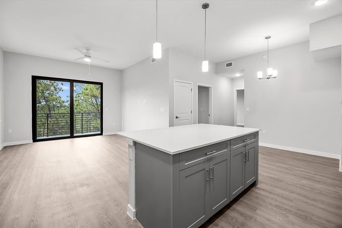 Modern apartment interior with open-plan living space, featuring a sleek kitchen island, hardwood floors, and large windows offering scenic views.