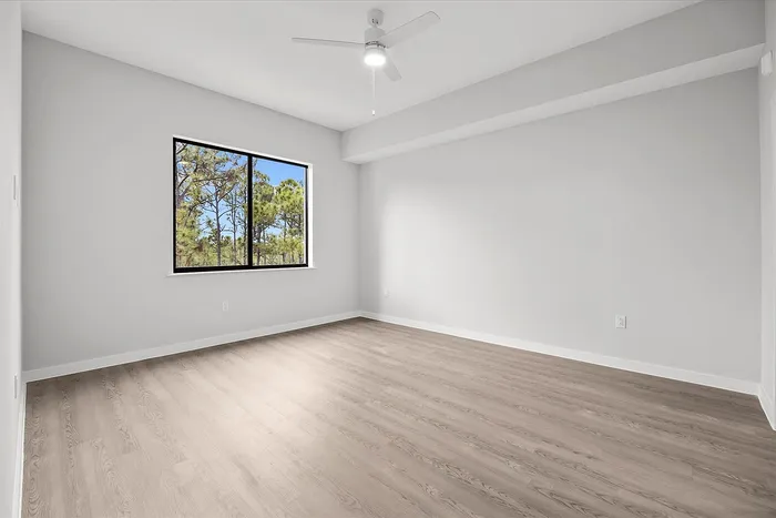 Bright and airy room with elegant flooring, a large window showcasing scenic greenery, and a modern ceiling fan for ultimate comfort.