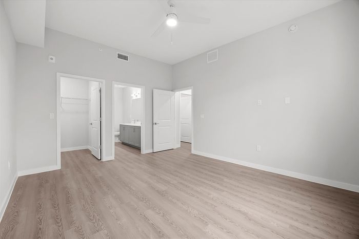 Bright and spacious room with elegant wood flooring, featuring an attached bathroom and a large closet.
