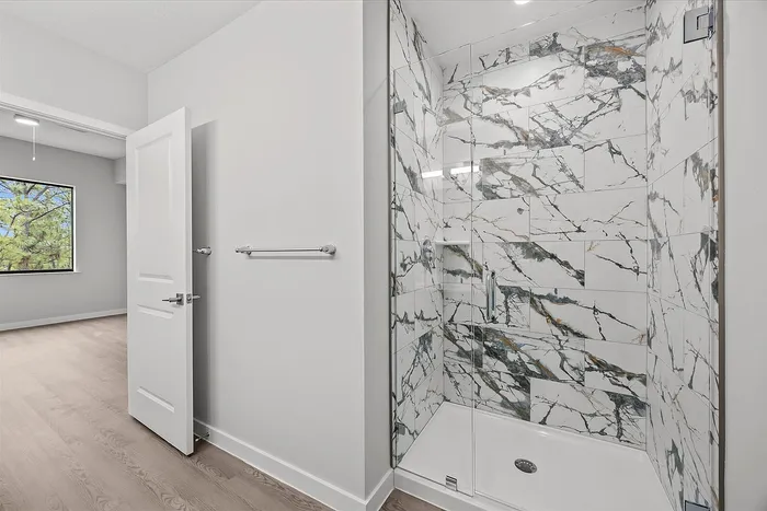Elegant bathroom with luxurious marble-tiled shower, modern fixtures, and sleek wood flooring, offering a serene and stylish retreat.