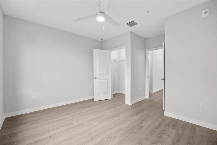 Bright and modern bedroom with sleek laminate flooring, ceiling fan, and spacious walk-in closet.