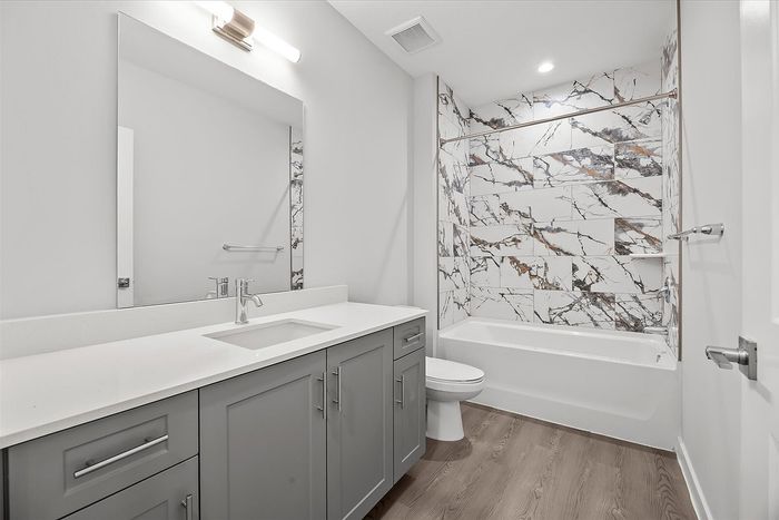 Elegant bathroom with modern gray vanity, sleek quartz countertop, and stylish marble-patterned tile in the shower.