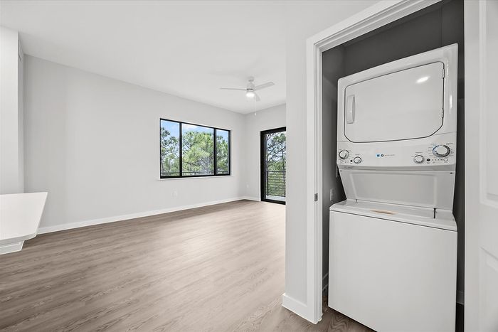 Bright and modern apartment room with large windows, wood flooring, and in-unit stacked washer and dryer.