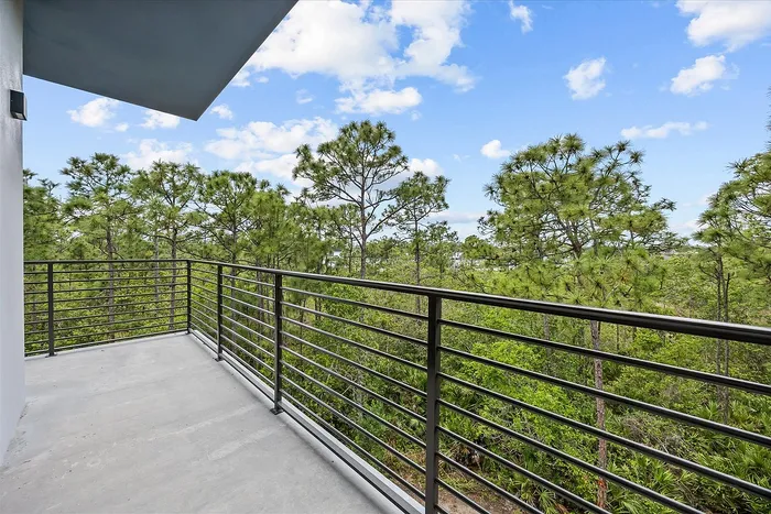 Inviting balcony with modern railing offering serene views of lush green trees and a clear blue sky.