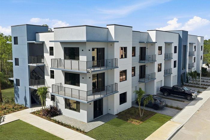 Modern three-story apartment complex with sleek balconies, spacious windows, and lush landscaping, showcasing contemporary architectural design.