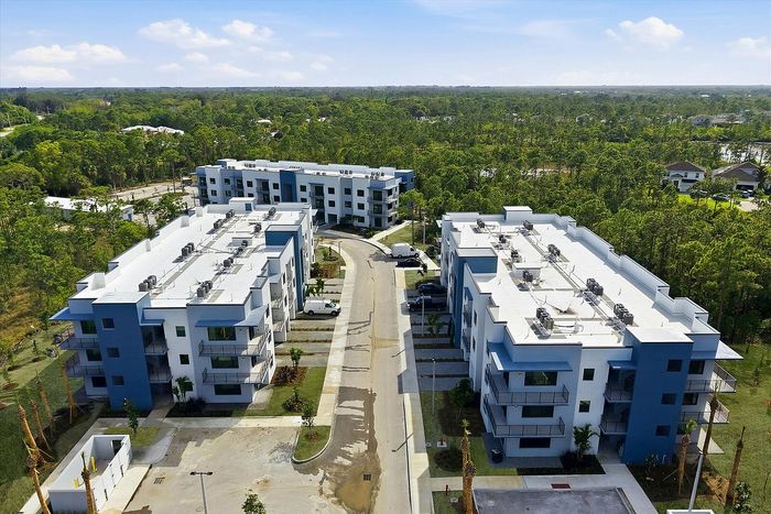 Modern apartment complex with striking blue accents, nestled amid lush greenery and offering ample parking space.