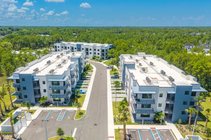Modern apartment complex with striking blue accents, nestled amid lush greenery and offering ample parking space.